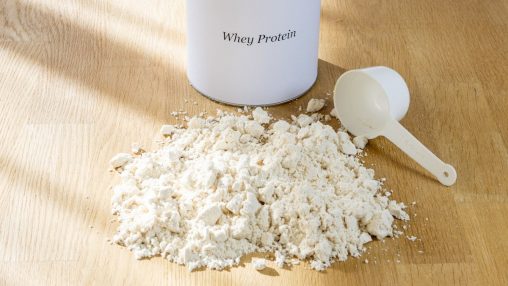 Whey protein powder with scoop on oak table in natural light, fitness lifestyle